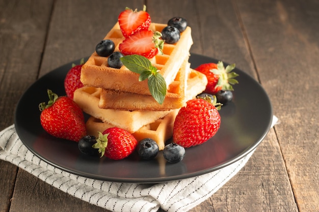 Frisches hausgemachtes Essen aus belgischen Beerenwaffeln mit Honig, Schokolade, Erdbeere, Blaubeere, Ahornsyr