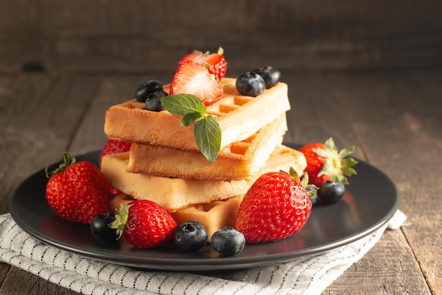 Frisches hausgemachtes Essen aus belgischen Beerenwaffeln mit Honig, Schokolade, Erdbeere, Blaubeere, Ahornsyr