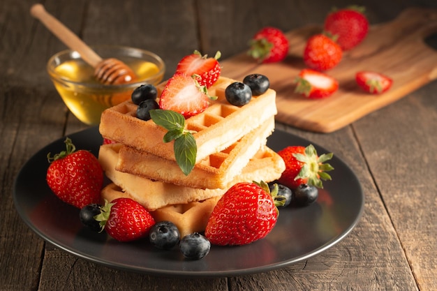 Frisches hausgemachtes Essen aus belgischen Beerenwaffeln mit Honig, Schokolade, Erdbeere, Blaubeere, Ahornsyr