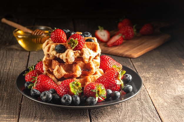 Frisches hausgemachtes Essen aus belgischen Beerenwaffeln mit Honig, Schokolade, Erdbeere, Blaubeere, Ahornsyr