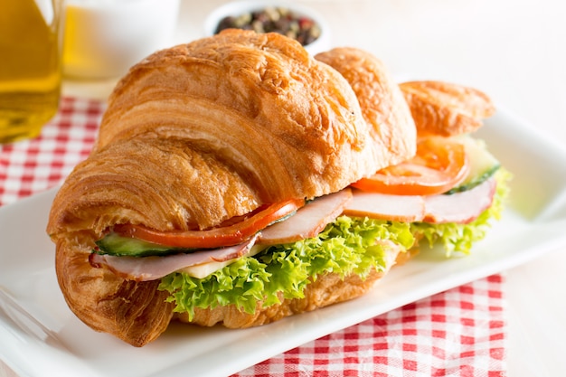 Frisches Hörnchen oder Sandwich mit Salat, Schinken auf hölzernem Hintergrund.