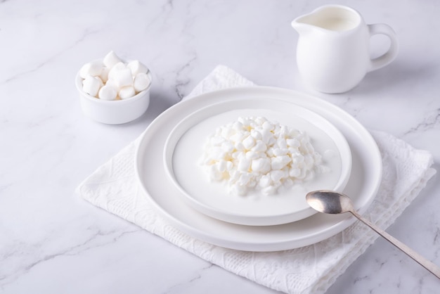 Frisches Hüttenkäsekorn in einer weißen Schüssel und Marshmallows Quark in Granulat mit Sahne Kopieren Sie Platz