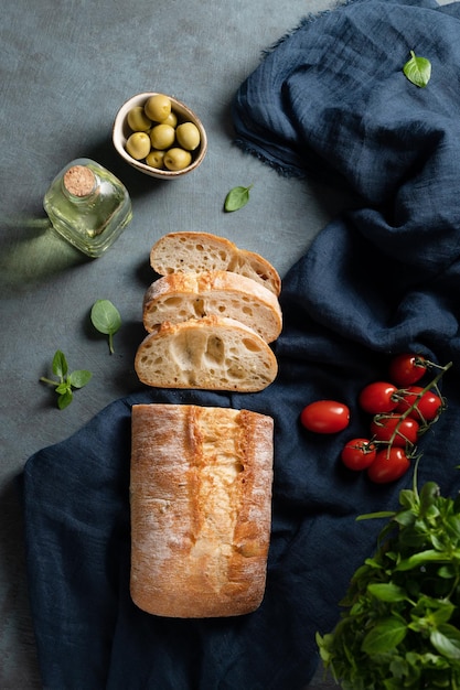 Frisches italienisches Ciabatta-Brot geschnittene Scheiben mit Tomaten-Basilikum und Oliven auf dunklem Hintergrund Draufsicht und Kopierbereich