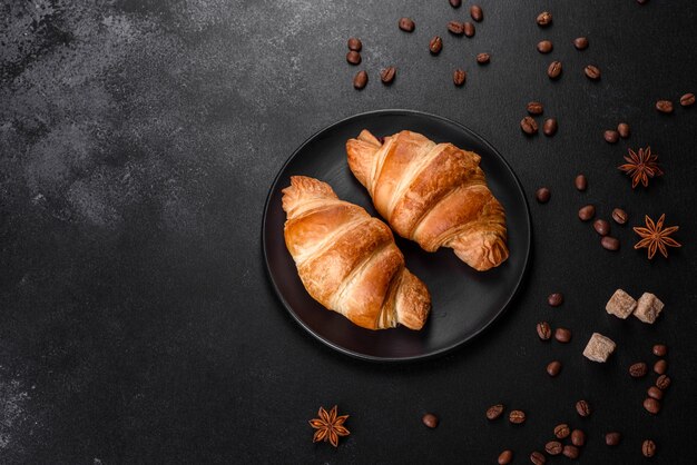 Frisches knuspriges köstliches französisches Croissant mit Kaffeebohnen auf schwarzem Tisch