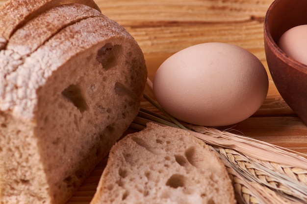 Frisches köstliches Brot, Konzept für das Backen. Eier in der Lehmschüssel- und -weizensprösslinge auf Holztisch