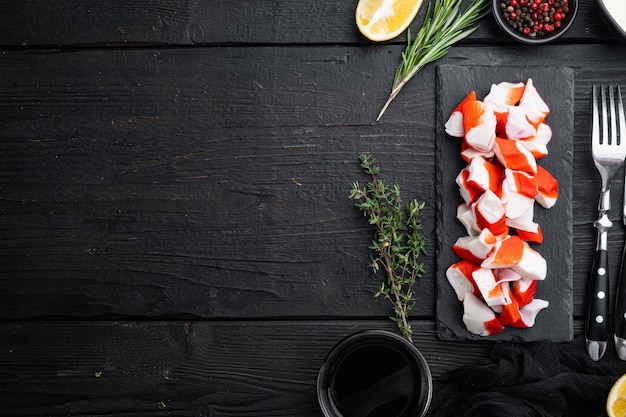 Frisches Krabbenfleischstäbchen-Surimi mit blauem Schwimmkrabbensatz, auf schwarzem Holztischhintergrund, Draufsicht flach, mit Copyspace und Raum für Text