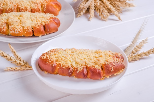 Frisches leckeres Brötchen mit Streuseln auf weißem Teller auf weißem Holzhintergrund