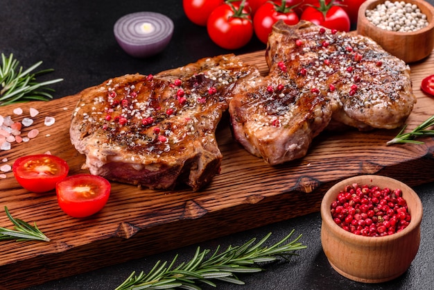 Frisches leckeres saftiges Steak auf den Knochen mit Gemüse und Gewürzen. Saftiger Schweinefleischsteakgrill auf dunklem Tisch