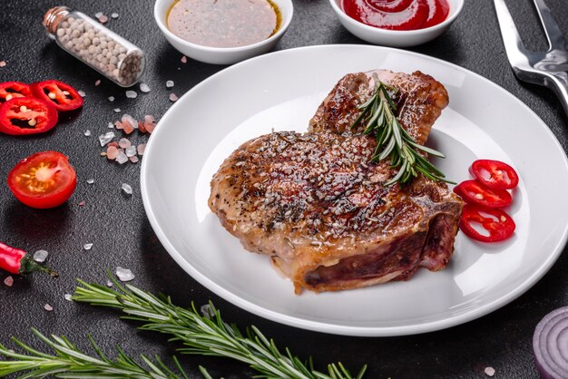 Frisches leckeres saftiges Steak auf den Knochen mit Gemüse und Gewürzen Schweinefleisch saftiges Steak Grill auf dunklem Tisch