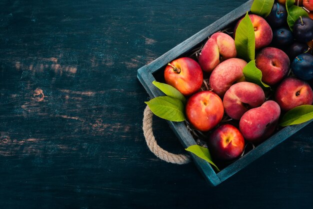 Frisches Obst in einer Holzkiste Aprikose Pfirsich Nektarine Pflaume Auf einem hölzernen Hintergrund Ansicht von oben Freier Platz für Ihren Text