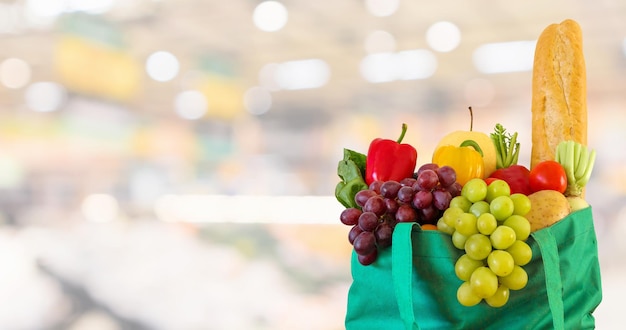 Frisches Obst und Gemüse in grüner Einkaufstasche mit unscharfem Hintergrund im Supermarkt-Lebensmittelgeschäft