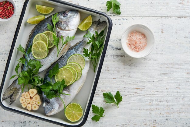 Frisches rohes Dorado mit Zitronenlime, Petersilie und Salz auf einem alten hölzernen weißen Hintergrund, bereit zum Kochen