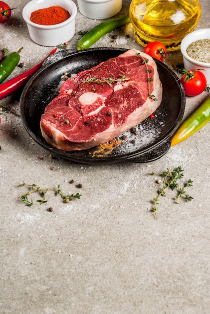 Frisches rohes Fleisch. Ein Stück Lammfilet, mit einem Knochen, mit einer Axt, mit Gewürzen zum Kochen auf grauem Steintisch