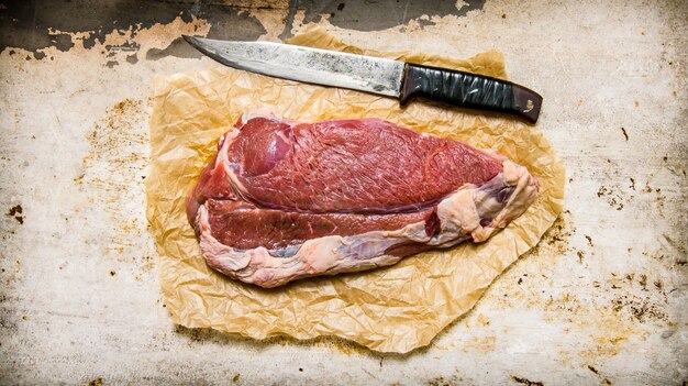 Frisches rohes fleisch mit einem fleischermesser. auf rustikalem hintergrund. draufsicht