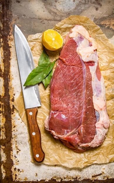 Frisches rohes Fleisch mit einem großen Messer und einem Lorbeerblatt.