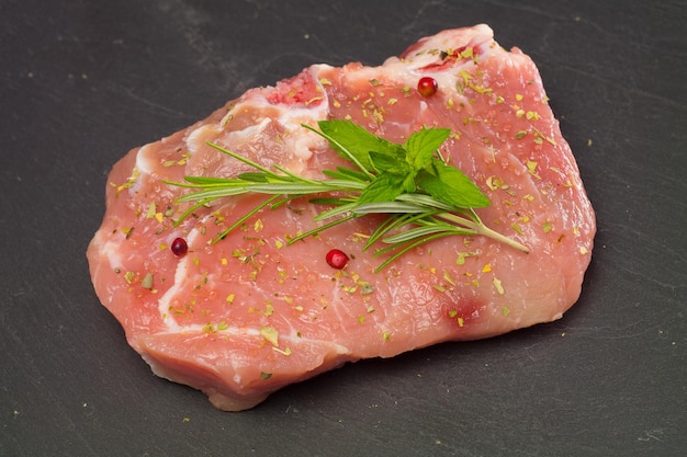 Frisches rohes Fleisch mit Rosmarin, Mentha und anderen Gewürzen auf grauer Steinplatte.