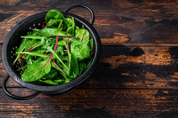 Frisches rohes gemischtes Grün, Spinat, Mangold und Rucola. Dunkler hölzerner Hintergrund. Ansicht von oben. Platz kopieren.