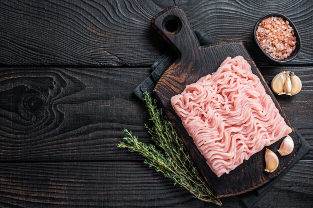 Frisches rohes Hackfleisch oder Hühnerfleisch auf Holzbrett mit Thymian. Schwarzer hölzerner Hintergrund. Ansicht von oben. Platz kopieren.