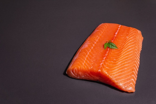 Frisches rohes Lachs- oder Forellenseefischfilet auf schwarzem Steinhintergrund. Nützliche Zutat für gesundes Essen, Quelle von Omega 3. Ein modernes hartes Licht, dunkler Schatten, kulinarische Tapete, Kopienraum