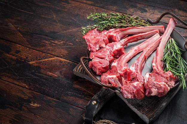 Frisches rohes Lammkotelettsteak in Stahlschale mit Kräutern Holzhintergrund Draufsicht Kopierbereich