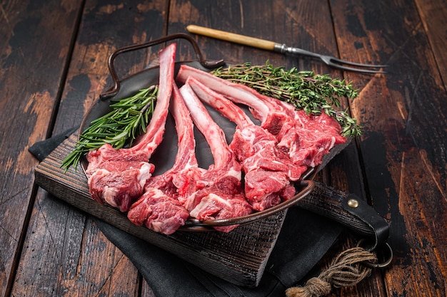 Frisches rohes Lammkotelettsteak in Stahlschale mit Kräutern Holzhintergrund Draufsicht