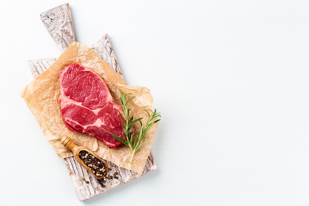 Frisches rohes Rib-Eye-Steak auf Holzschneidebrett mit Spinat, Linsen und Rosmary im rustikalen Stil.