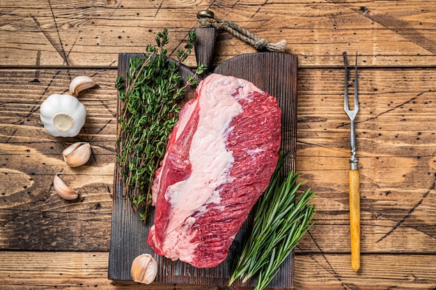 Frisches rohes Rinderbrustfleisch, das auf einem Holzbrett mit Kräutern erstklassig geschnitten wird. hölzern