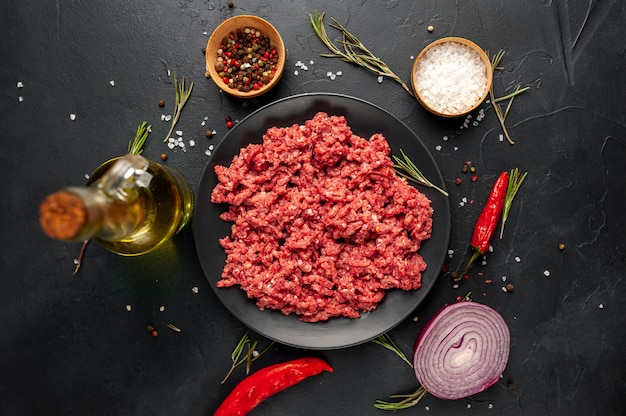 Frisches rohes Rinderhackfleisch mit Kräutern und Gewürzen auf einem schwarzen Teller auf einem Steinhintergrund