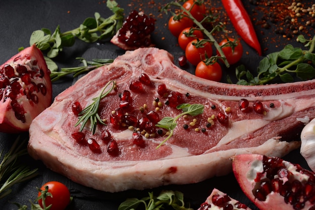 Frisches rohes Rinderknochenrippensteak auf schwarzem Brett mit Kräutern und Gewürzen