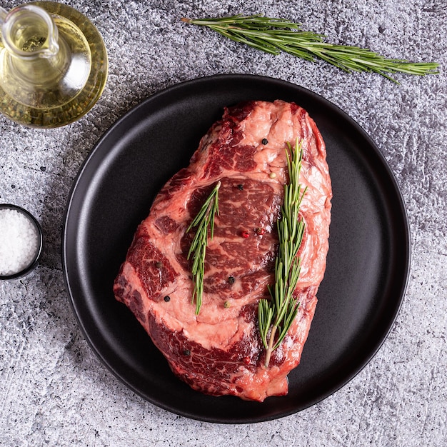 Frisches rohes Rindersteak auf schwarzem Teller, Ansicht von oben.