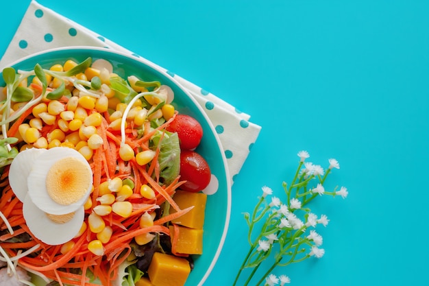 Frisches Salatgemüse mit gekochtem Hühnerei und verzierter Blume auf blauem Hintergrund