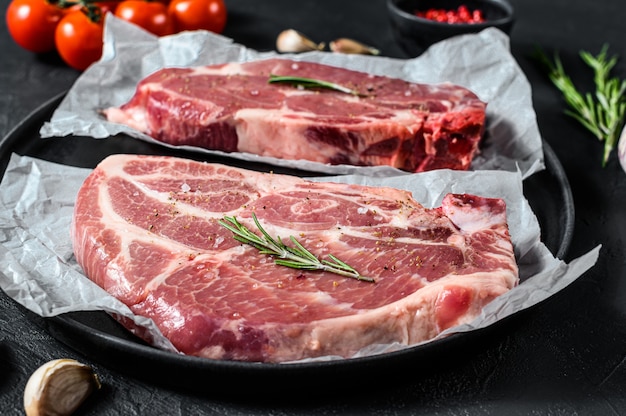 Frisches Schweinesteak. Marmorfleisch auf Pergamentpapier. Schwarzer Hintergrund. Ansicht von oben