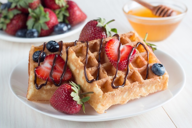 Frisches selbst gemachtes Lebensmittel von belgischen Waffeln der Beere mit Honig, Schokolade, Erdbeere, Blaubeere, Ahornsirup und Creme. Gesundes Nachtischfrühstückskonzept mit Saft