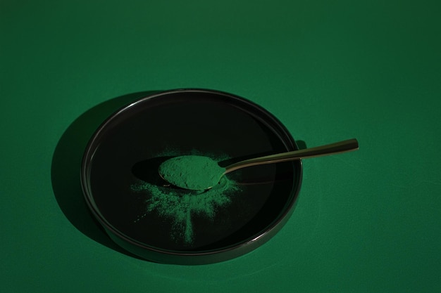 Frisches Spirulina-Algenpulver auf einem Löffel auf schwarzem Hintergrund auf grünem Hintergrund Bio-Spirulina-Pulver