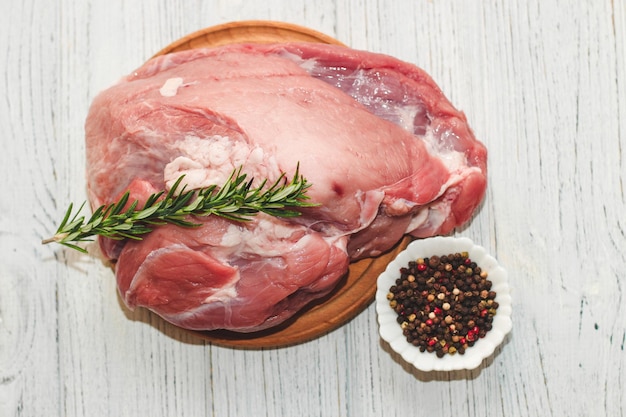 Frisches Stück Fleisch großer Schweineschinken auf einem Brett mit Pfeffer und Rosmarin