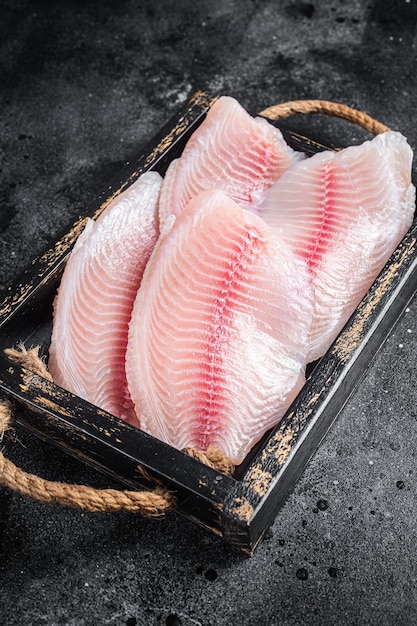 Frisches Tilapia-Weißfischfilet in einem Holztablett Schwarzer Hintergrund Draufsicht