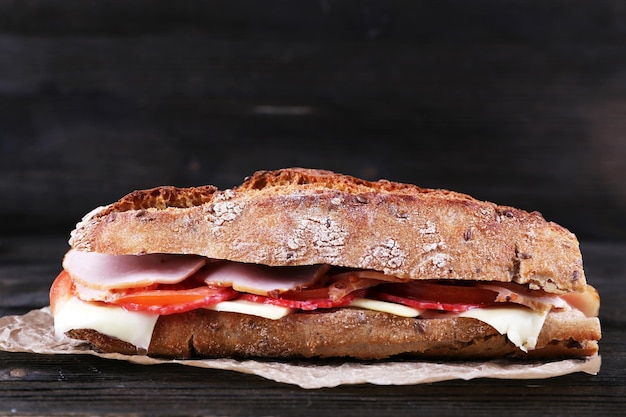 Foto frisches und leckeres sandwich mit schinken und käse auf papier auf holzgrund