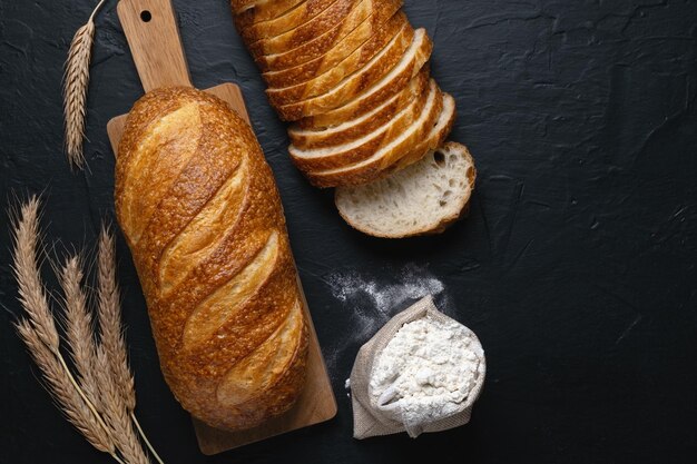 Frisches Weizenbaton-Brot und Mehl auf dunklem HintergrundDraufsicht Kopieren Sie Platz