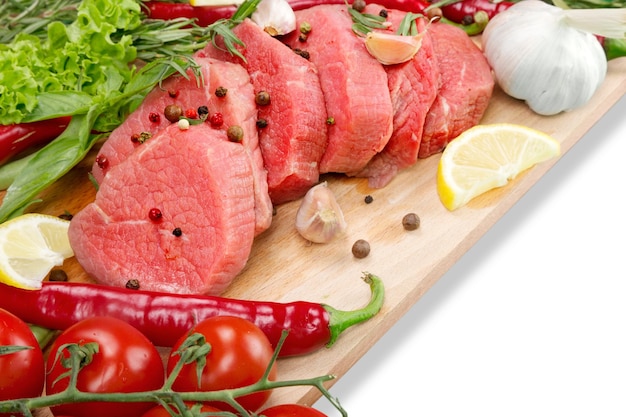 Frischfleisch - frische Steaks auf einer gelben Matte, frische Kräuter und Gemüse isoliert auf weißem Hintergrund