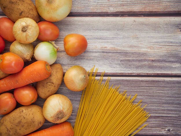 Frischgemüse, das eine Mischung von Spaghettis ist, briet die Zwiebeln, die Karotten, die Kartoffeln, die Tomaten, gesetzt auf einen alten Holztisch. Ansicht von oben