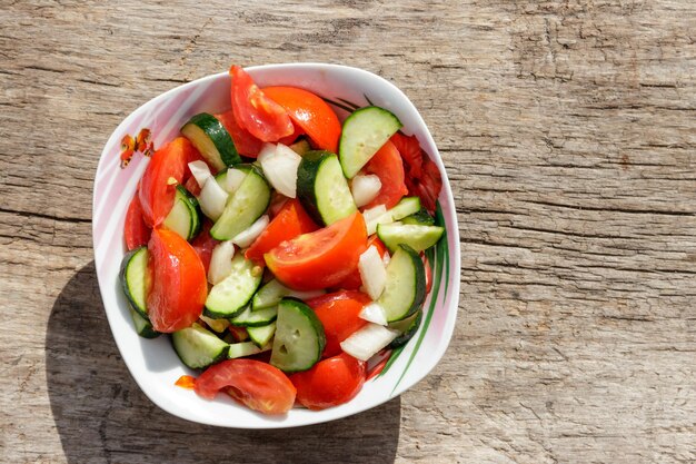 Frischgemüsesalat mit Tomaten, Gurken, Zwiebeln und Olivenöl auf Holztisch. Ansicht von oben