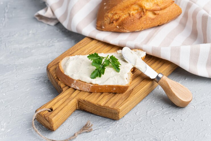 Frischkäse mit Kräutern und Gewürzen auf einer Scheibe frischem, knusprigem Roggenbrot mit Käsemesser in der Nähe
