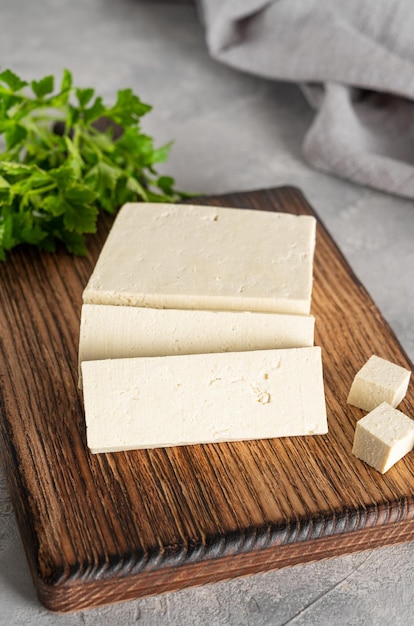 Frischkäse-Tofu aus Sojabohnen mit Petersilie auf einem Brett auf grauem Hintergrund Ein veganes Produkt