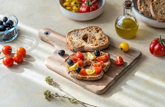 Friselle sind typisch italienisches, doppelt gebackenes Brot, hier belegt mit roten und gelben Tomaten, Olivenöl, Oliven und Oregano auf einem Schneidebrett