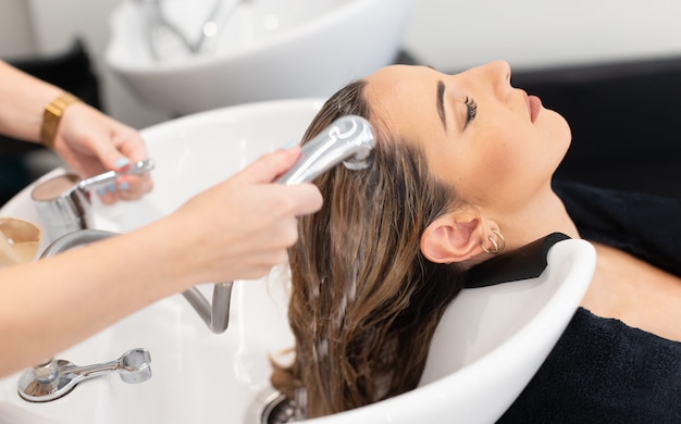 Friseur bei der Arbeit Friseur, der der Kundin blonde Haare mit geschlossenen Augen wäscht