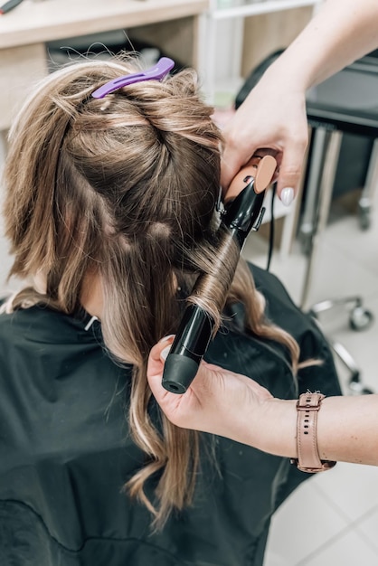 Friseur bereitet Frau vor, macht Lockenfrisur mit Lockenstab Langes hellbraunes Naturhaar