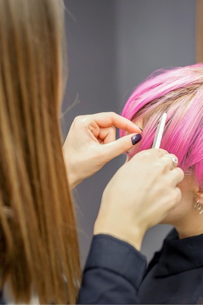 Friseur bereitet gefärbte kurze rosa Haare einer jungen Frau auf Eingriffe in einem Schönheitssalon vor.