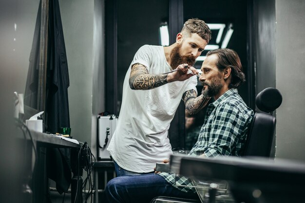 Friseur beugte sich zu seinem Klienten, während er eine Schere hielt und seinen Bart kämmte