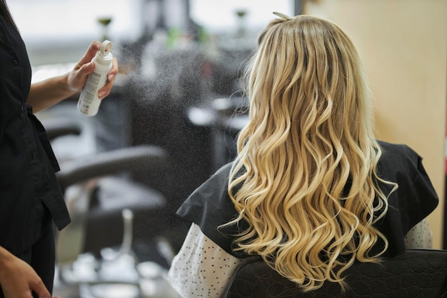 Friseur, der das lange blonde Haar der Frau mit Haarspray besprüht, Nahaufnahme
