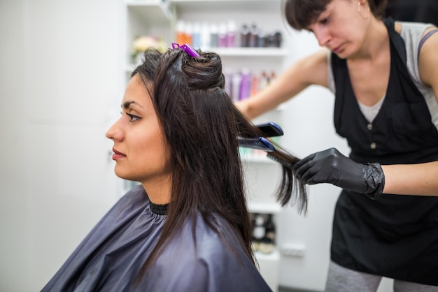 Friseur, der ein Haar begradigt, um das Haar zu begradigen Friseur, der an der Frisur einer Frau im Salon arbeitetHaarpflege Schöne, attraktive Frau in einem Schönheitssalon